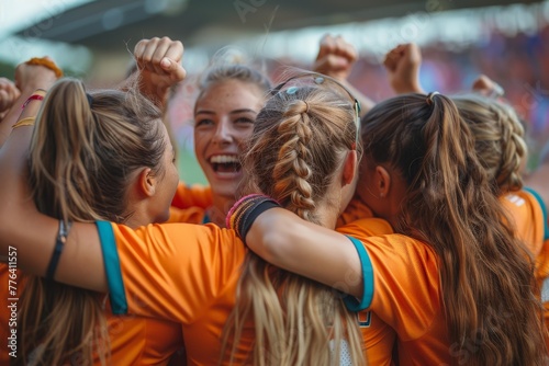 Women's football team in orange jerseys huddling and expressing joy, likely after winning a game or match