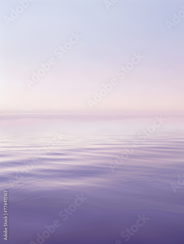 A calm body of water with a light blue sky in the background. The water is still and the sky is a soft, pastel color