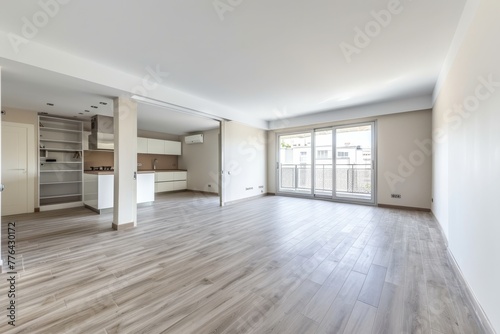Interior of empty spacious living room with white walls and laminated floor with doors leading to balcony