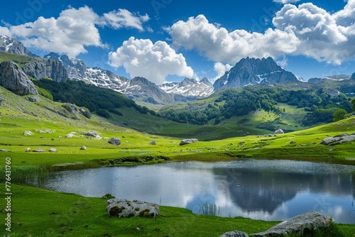 Scenic view of a mountain range with green grass and a pond under a cloudy blue sky during daylight