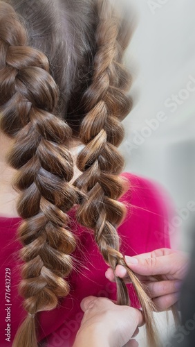 Hairdresser weaves a braid to a preteen blond girl in a beauty and hair salon with motion blur effect