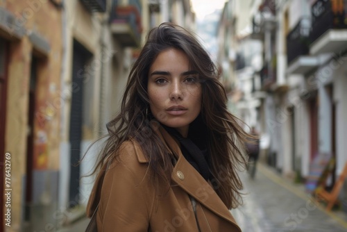 Serious hispanic female with long hair in stylish outfit looking at camera while standing on street with buildings in city