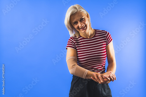 young woman with a bandage on her elbow for support, blue background. High quality photo