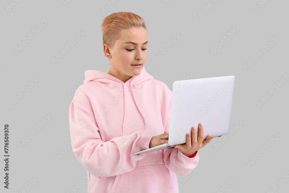 © Pixel-Shot - Young woman with short hair using laptop on grey background © Pixel-Shot - Young woman with short hair using laptop on grey background