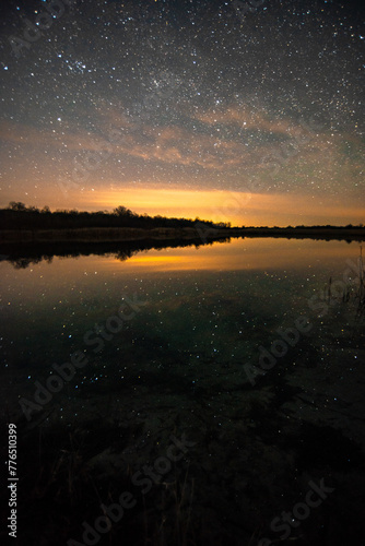 Stars on lake . Night over the lake . Yellow light over the forest . Stars on water. Reflaction 