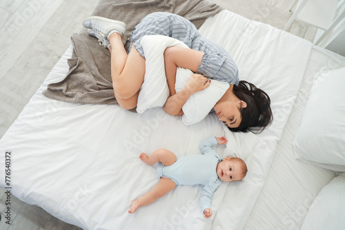 Young woman with her baby suffering from postnatal depression on bed, top view