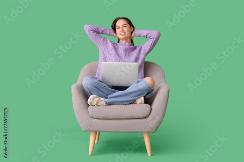Beautiful young happy woman with laptop resting on armchair against green background © Pixel-Shot