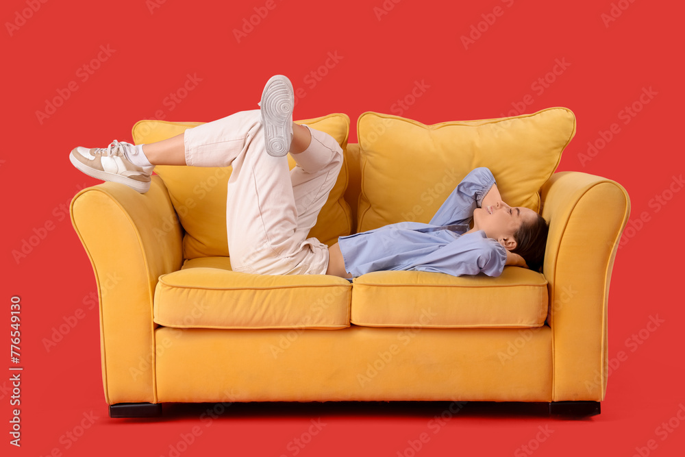 Beautiful young woman resting on sofa against red background