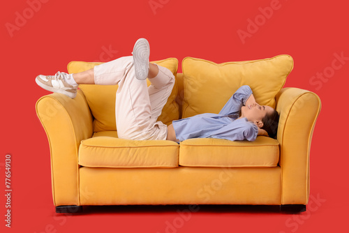 Beautiful young woman resting on sofa against red background © Pixel-Shot