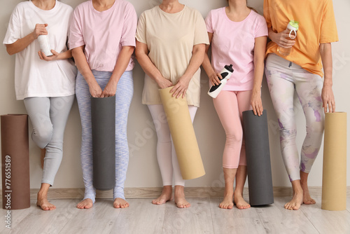 Group of mature women with yoga mats and water bottles near light wall