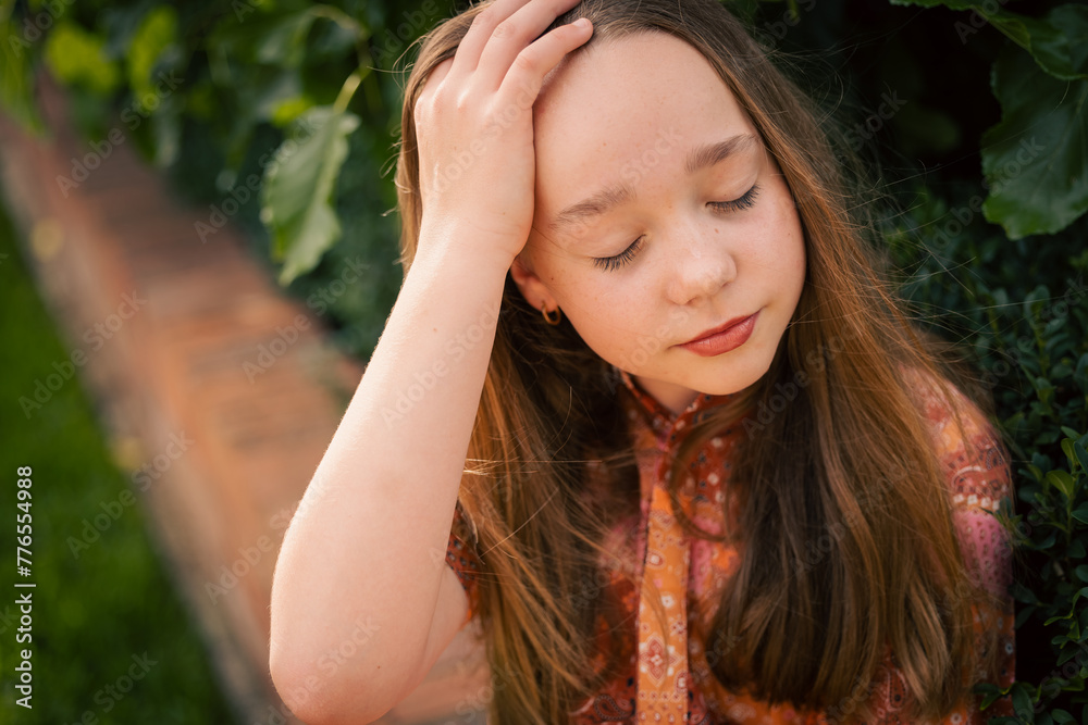 Portrait of pre-teen girl sitting on brick wall with natural green leafy background
