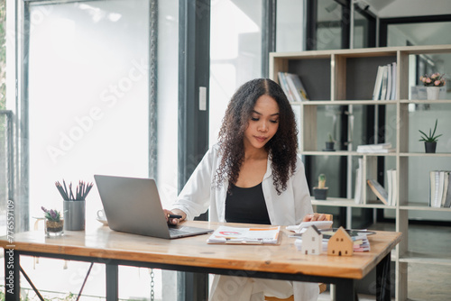 Real estate agent attentively examines property listings on her laptop in a stylishly furnished office, symbolizing professionalism and dedication.