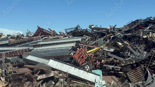 Panning shot over an industrial scrapyard. Heaps of wasted metal are being organized for recycling by heavy machinery.