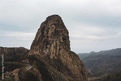 Majestic rock formation resembling a giant standing tall amidst the rugged mountains under a dramatic cloudy sky, creating a breathtaking and awe-inspiring sight for visitors