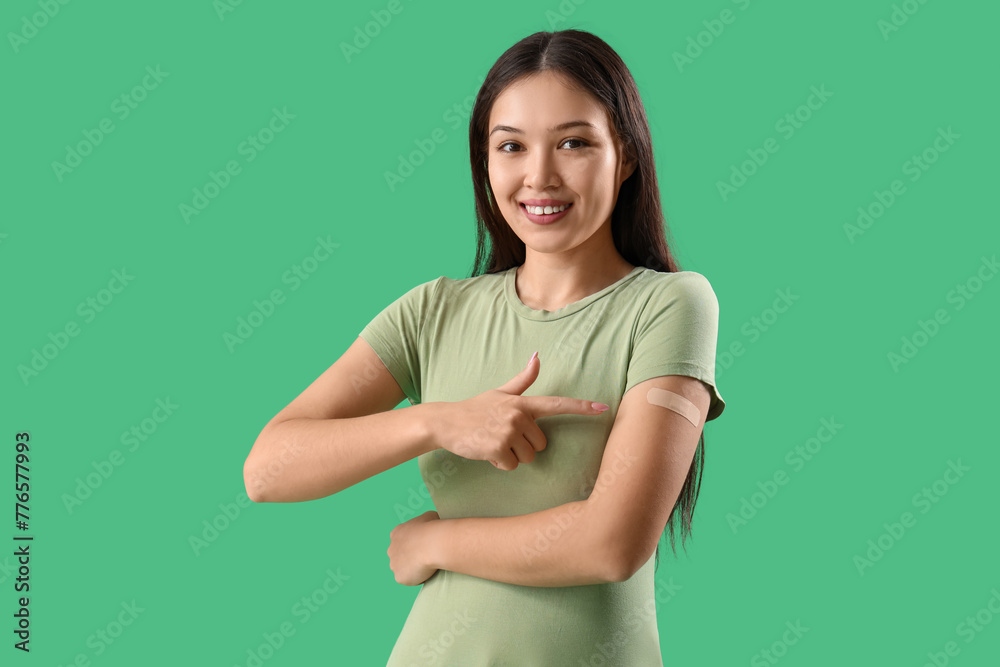 Beautiful young woman pointing at applied medical patch on her arm against green background Beautiful young woman pointing at applied medical patch on her arm against green background
