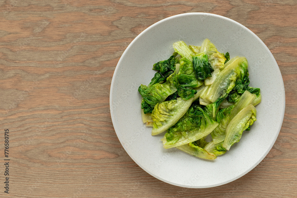Stir-fried lettuce on a plate. Cherished prosperity dish served around Chinese New Year. Wooden surface with copy space. Stir-fried lettuce on a plate. Cherished prosperity dish served around Chinese New Year. Wooden surface with copy space.