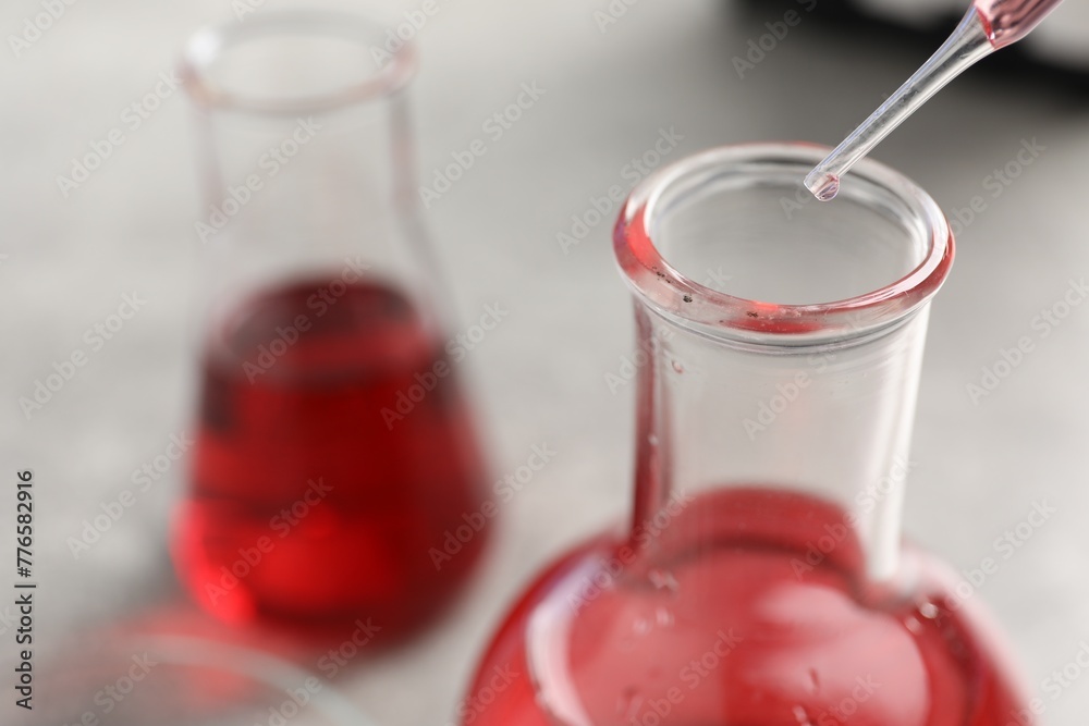 Laboratory analysis. Dripping red liquid into flask at light grey table, closeup Laboratory analysis. Dripping red liquid into flask at light grey table, closeup