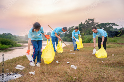 group of volunteers in blue t-shirt collecting garbage and sorting plastic waste, voluntary asian family team cleanup dirty camping area full of garbang by the river