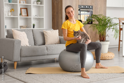 Young pregnant woman with cat sitting on fitball at home