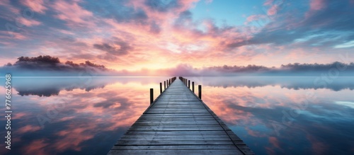 The wooden dock is stretching out into the calm waters as the sun rises in the horizon, creating a tranquil and picturesque scene