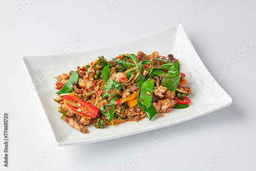 Stir fried spicy Frog leg with vegetables and herbs (chilli, galangal, kaffir lime leaves and basil) served on white plate isolated on white background.