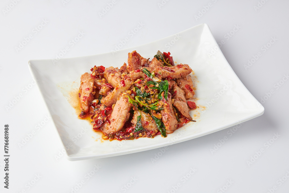 Thai spicy stir-fried grilled pork neck (Pork Jowl) with holy basil leaves served in white plate isolated on white background. Hot and spicy.