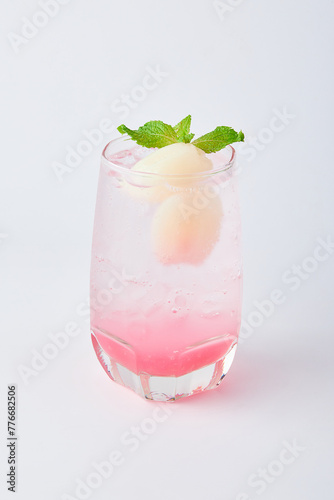 Refreshing Lychee Soda with ice topped with fresh lychee and mint served in a clear glass isolated on white background.