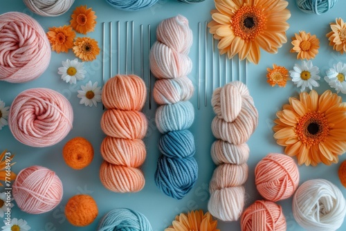 Overhead view of a crafting setup with colorful yarn balls, knitting needles, and daisies on a blue background.
