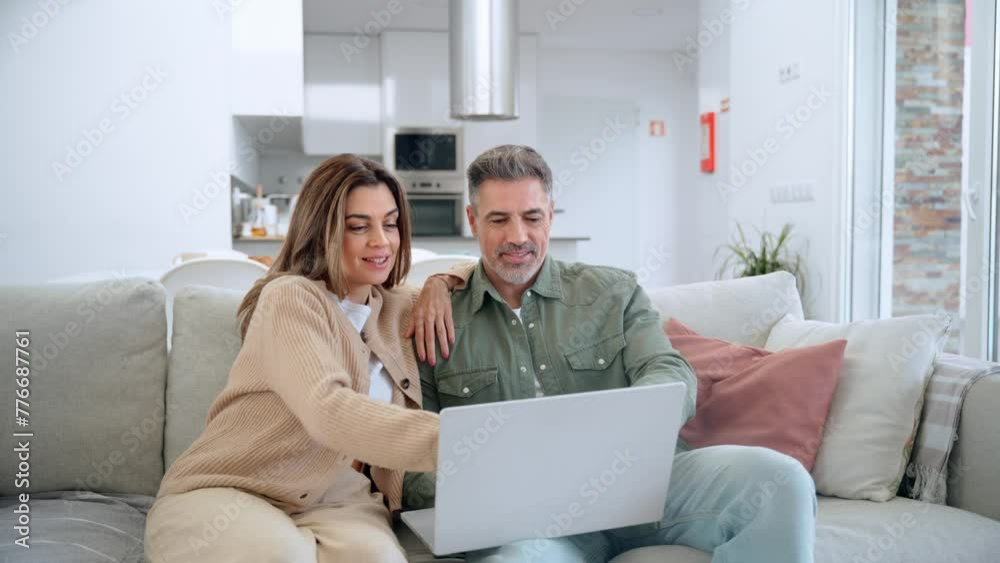 Happy middle aged couple using laptop relaxing on couch at home. Smiling mature man and woman looking at computer watching video, browsing or shopping in ecommerce store sitting on sofa in living room Happy middle aged couple using laptop relaxing on couch at home. Smiling mature man and woman looking at computer watching video, browsing or shopping in ecommerce store sitting on sofa in living room