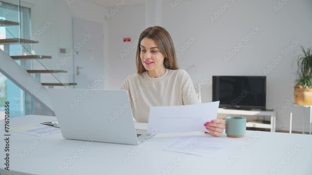 Happy middle aged woman looking at laptop holding documents hybrid working at home table. Mature lady paying bills online checking financial papers invoice making baking payments using computer. Happy middle aged woman looking at laptop holding documents hybrid working at home table. Mature lady paying bills online checking financial papers invoice making baking payments using computer.