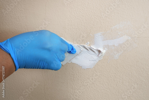 Hand in a blue glove uses a spatula to smear putty