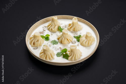 Khinkali with meat in cream sauce with parsley in a round plate on a black background. Food photos.