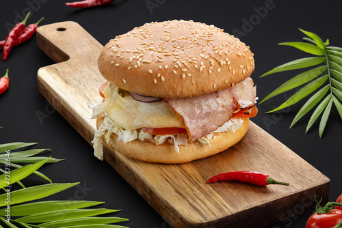 A big burger with bacon.with melting cheese, tomatoes, onions and vegetables on a wooden board.Dark background. Food photos. Advertising for the menu.