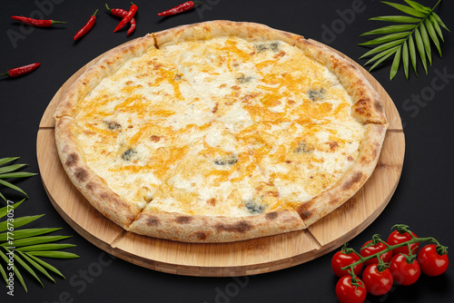 Pizza with several types of cheeses on a round wooden board on a black background with tomatoes and peppers. Food photos. View from above.