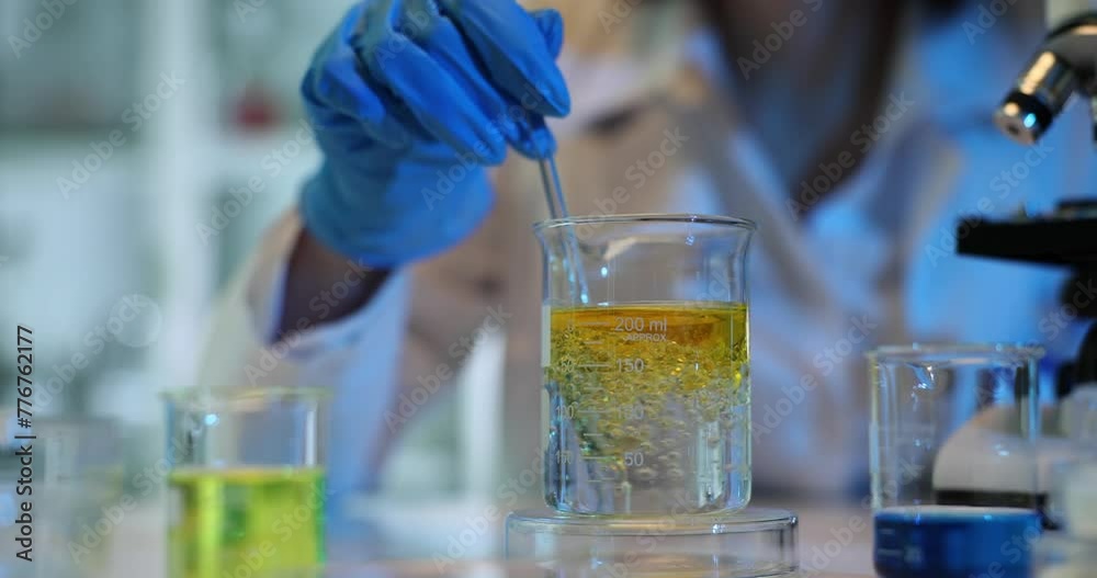 Scientist wearing gloves mixes two liquids in glass beaker with glass rod Scientist wearing gloves mixes two liquids in glass beaker with glass rod