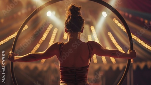 A female circus performer back to the camera crouches on the edge of the ring with a hoop in hand ready to captivate the audience . .