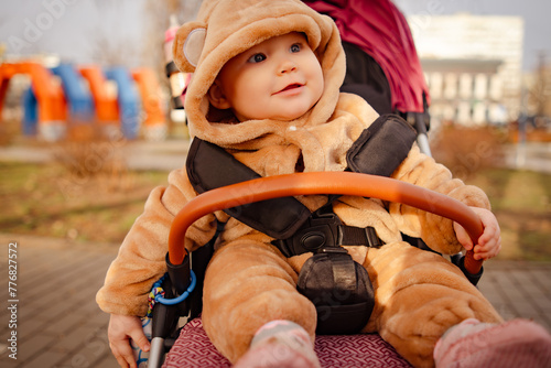A small child dressed in a bear costume playfully rides in a stroller, creating a cute and whimsical scene.