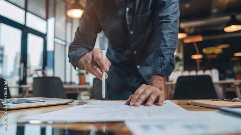 Focused professional examining and pointing to business reports on a wooden desk in a modern office setting.. Focused professional examining and pointing to business reports on a wooden desk in a modern office setting..