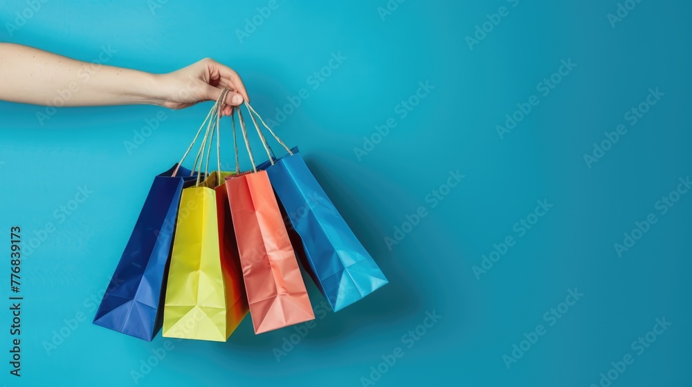 man hand holding many colorful shopping bags on blue background