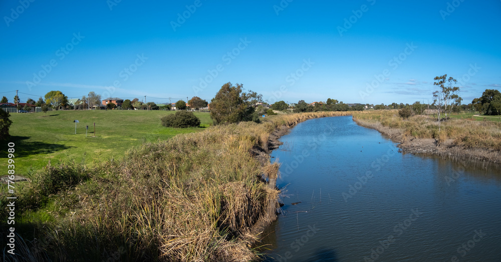 A panoramic vista of Skeleton Creek wetlands, the vastness of the Australian landscape, with still water reflecting a clear blue sky, houses in the distance. Copy space for text. A panoramic vista of Skeleton Creek wetlands, the vastness of the Australian landscape, with still water reflecting a clear blue sky, houses in the distance. Copy space for text.