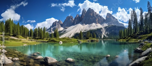 Tranquil alpine lake encircled by jagged rocks and lush green trees in the foreground with a serene mountain backdrop