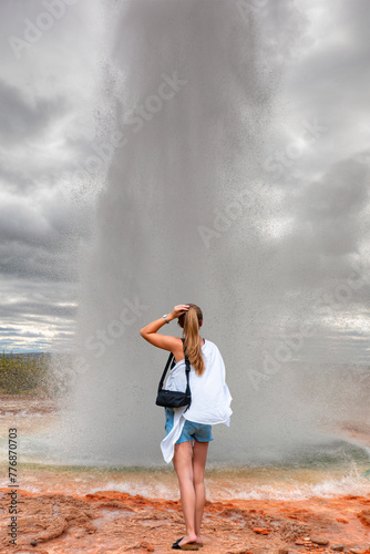 A beautiful young blonde girl wearing mini shorts is watching the view - Eruption of Strokkur Geyser - Haukadalur Valley, Iceland