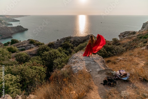 Woman sunset sea red dress, back view a happy beautiful sensual woman in a red long dress posing on a rock high above the sea on sunset. © svetograph