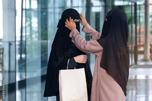 Muslim woman checks her friend's hijab while walking around the city