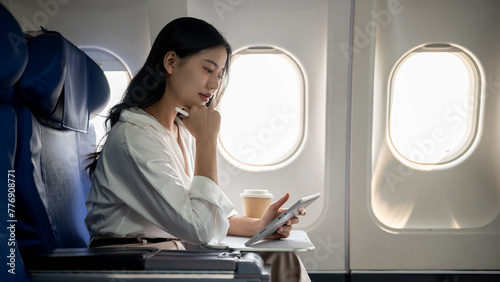 An attractive, hard-working Asian businesswoman is working on her tablet while traveling by plane.