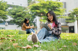 A female college student is studying on her digital tablet while sitting on grass in a park.