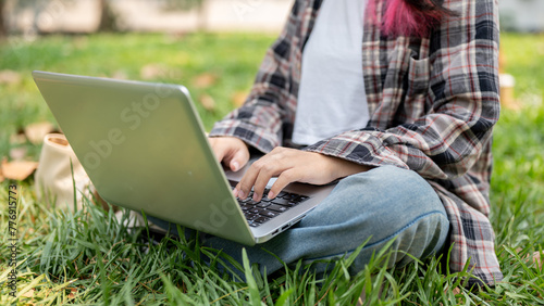 A cropped image of a female using her laptop computer while sitting on the grass in a park.