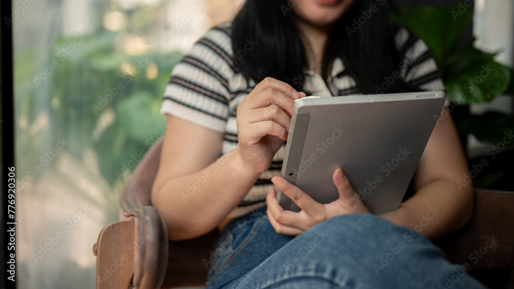 A cropped shot of an Asian woman using her digital tablet in a vintage green coffee shop. A cropped shot of an Asian woman using her digital tablet in a vintage green coffee shop.