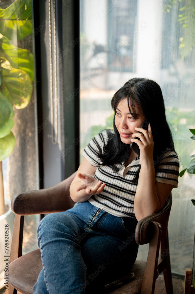 A positive Asian woman is talking on the phone with someone while sitting in a coffee shop. A positive Asian woman is talking on the phone with someone while sitting in a coffee shop.