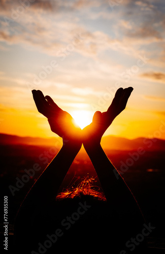 A child's hands holding the sun in silhouette while forming a V-shape, backlit by the sunset behind.